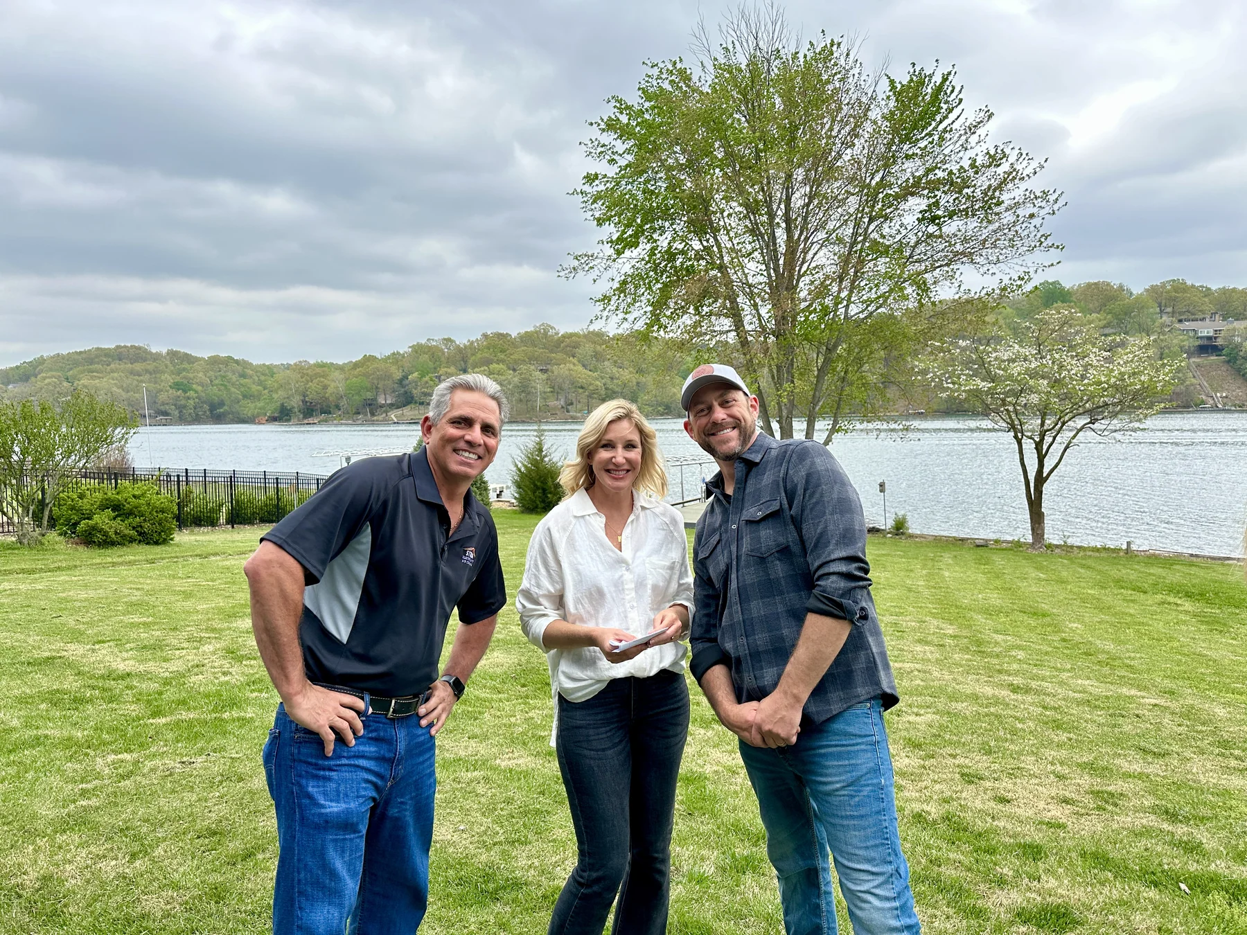 Joe Strada standing with two neighbors on a lawn beside a lake
