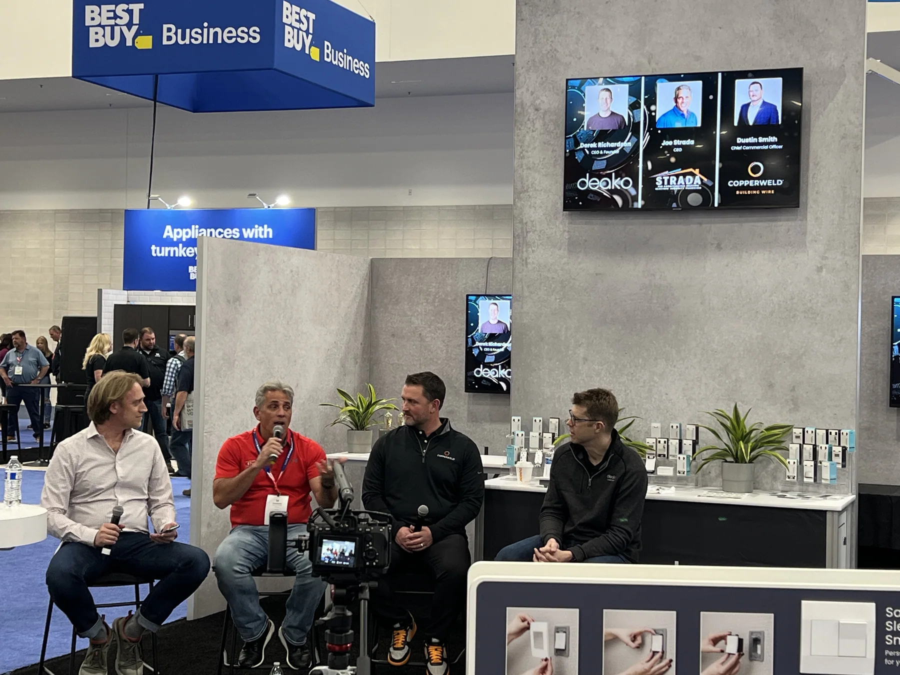 Panel discussion on a conference stage in front of a business exhibit booth