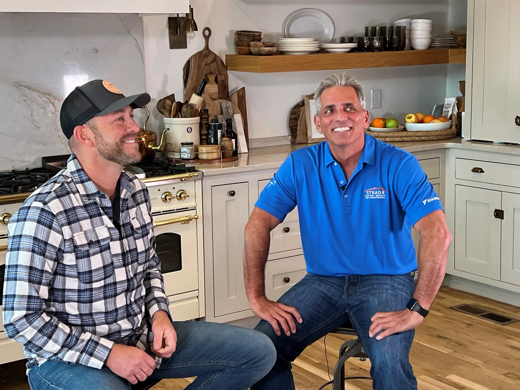 Joe Strada seated in a bright kitchen talking with a homeowner in a plaid shirt