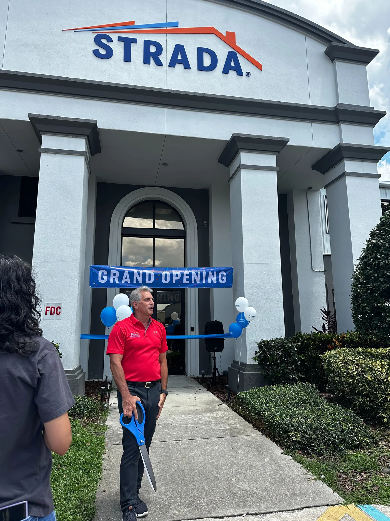 Joe Strada holding scissors at a Grand Opening ribbon cutting outside a Strada building