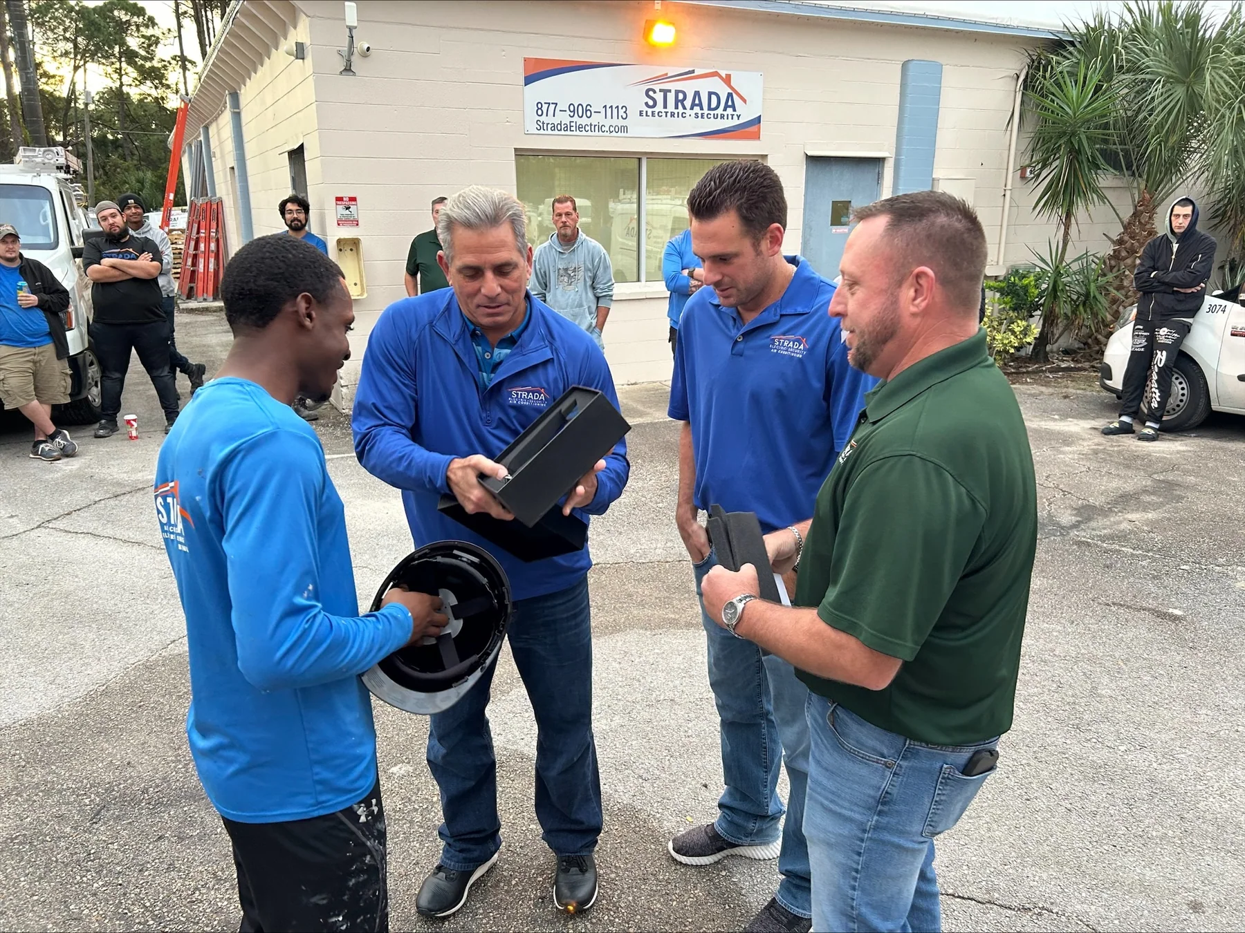 Joe Strada handing equipment to a crew member while a group of team members gathers outside a Strada facility